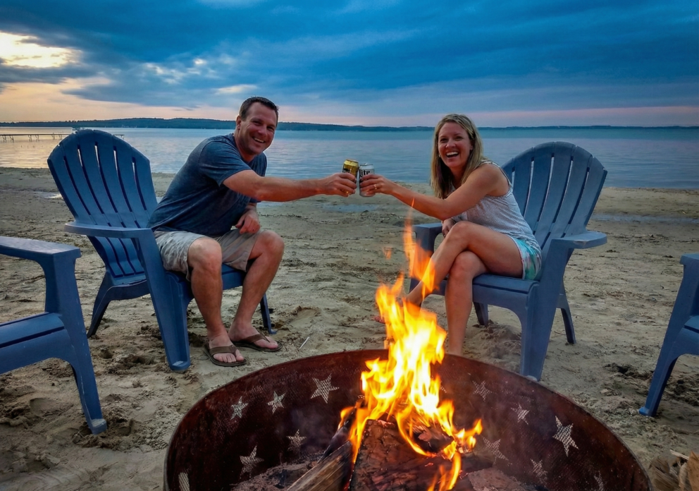 a man and woman sitting on chairs at a beach with a fire pit